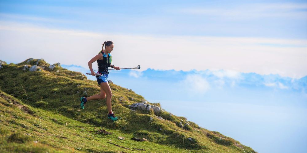 A woman is running up a grassy hill with a pole.