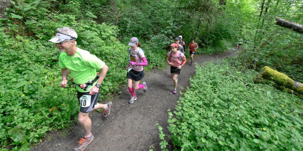 A group of people are running down a trail in the woods.