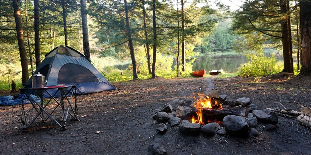 A tent is sitting next to a fire pit in the middle of a forest.