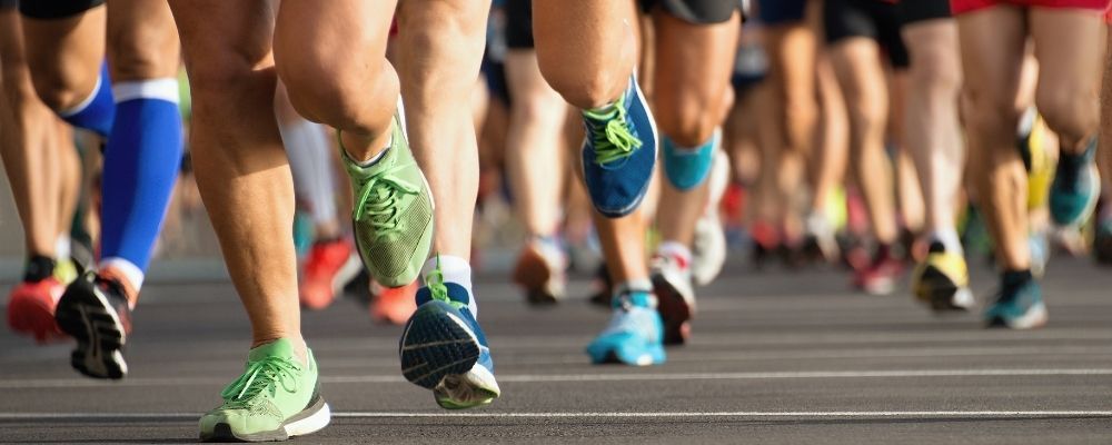 Runners' legs and feet, blurred background. Several pairs of running shoes in focus on a grey road.