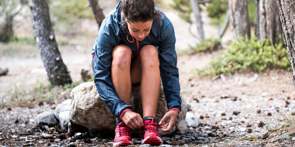 woman sitting down tying her trail running shoes