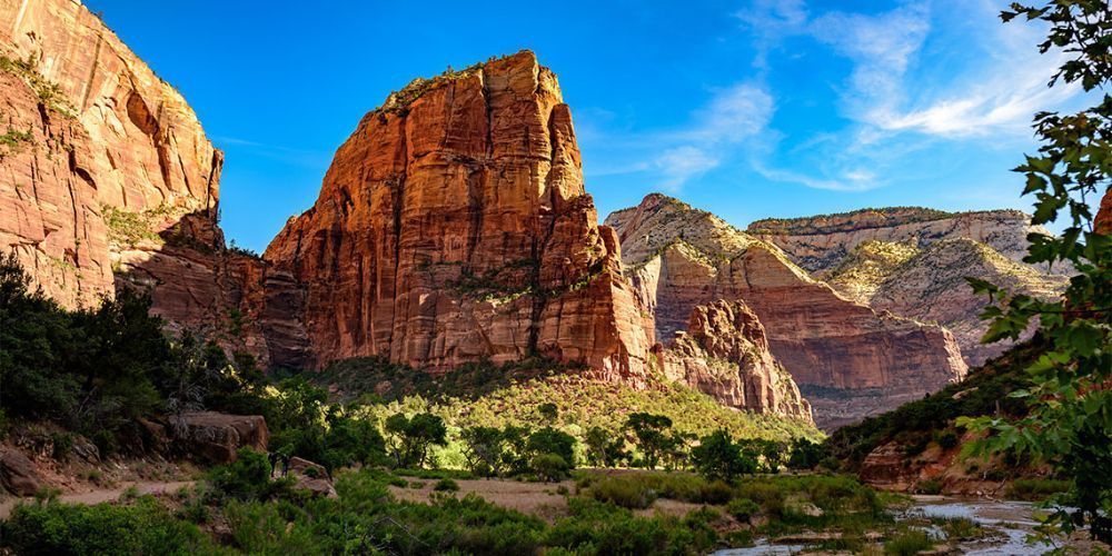 A large rock formation in the middle of a canyon with a river in the foreground.