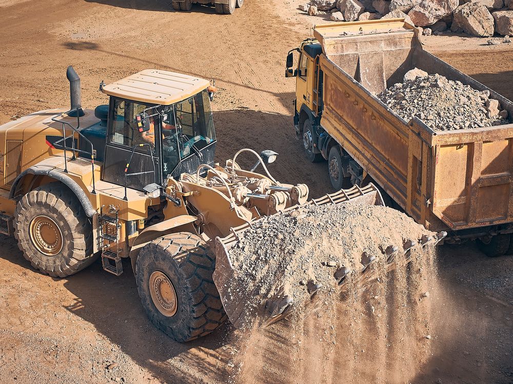 Yellow Loader Dumping Gravel Into a Dump Truck in a Quarry — Paul’s Tyres & Farm Maintenance in Apsley, NSW