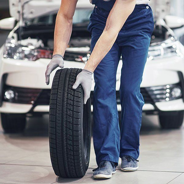 Mechanic in Blue Uniform, Lifting a Tire — Paul’s Tyres & Farm Maintenance in Apsley, NSW