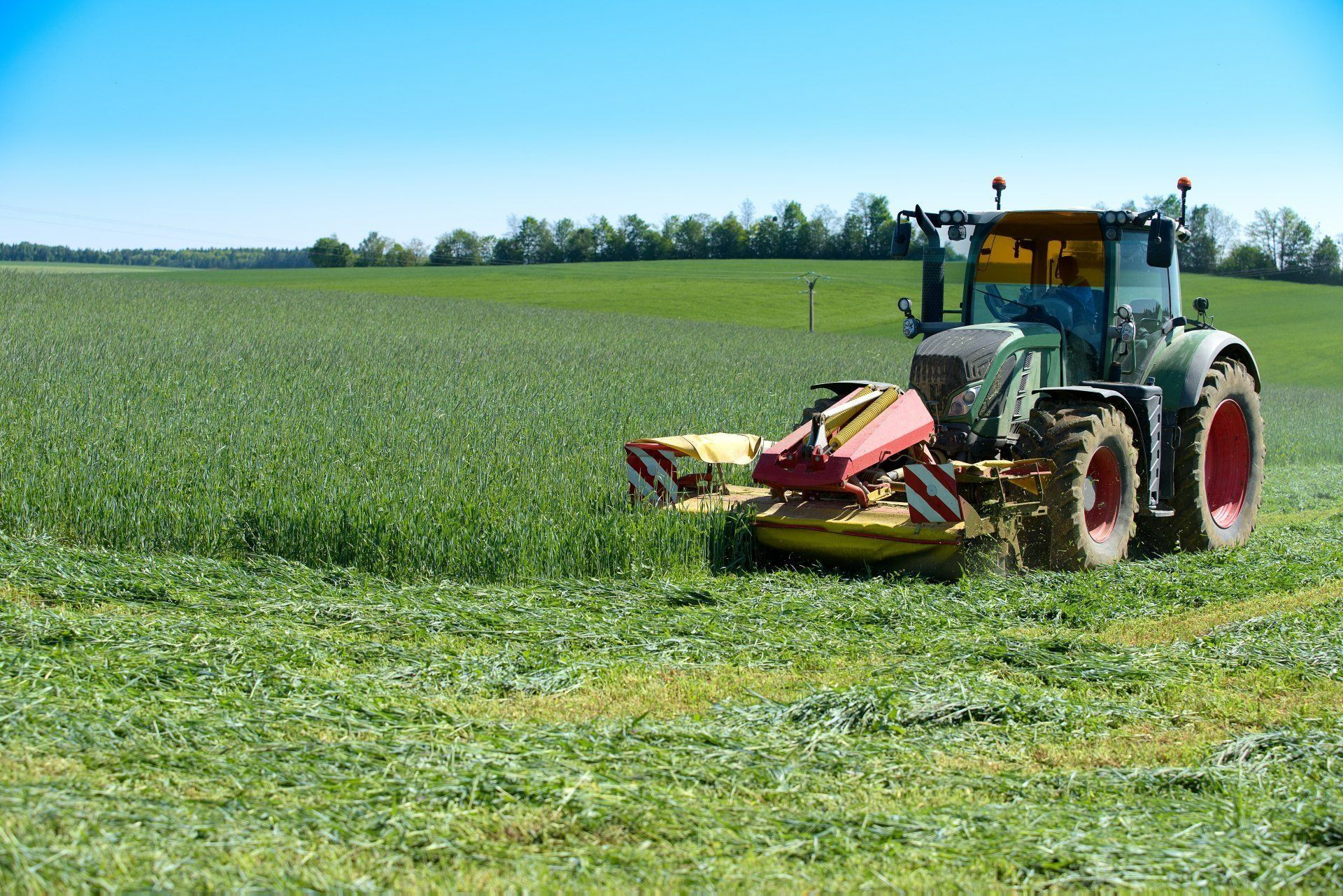 Tractor Mowing a Green Field Under a Blue Sky — Paul’s Tyres & Farm Maintenance in Apsley, NSW