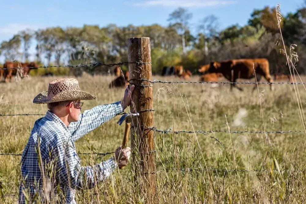 A Person in a Hat Repairs a Barbed-wire Fence — Paul’s Tyres & Farm Maintenance in Apsley, NSW