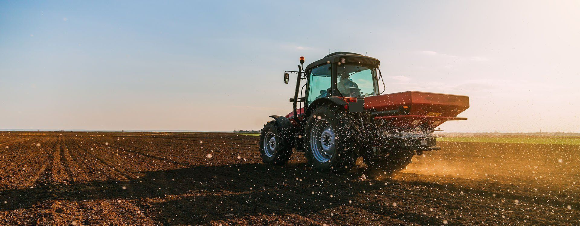 A Tractor Spreading Fertilizer Across a Freshly Plowed Field — Paul’s Tyres & Farm Maintenance in Apsley, NSW