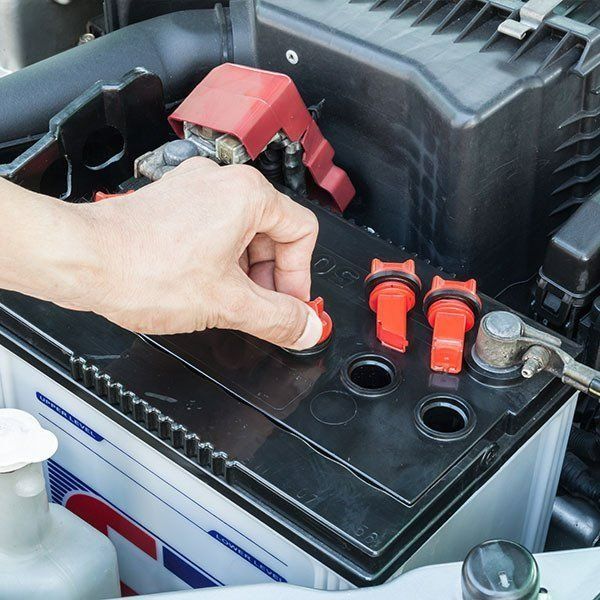 Hand Removing a Red Cap From a Car Battery. Engine Bay Setting — Paul’s Tyres & Farm Maintenance in Apsley, NSW