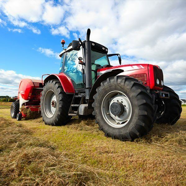 Red Tractor Baling Hay in a Field on a Sunny Day — Paul’s Tyres & Farm Maintenance in Mudgee, NSW