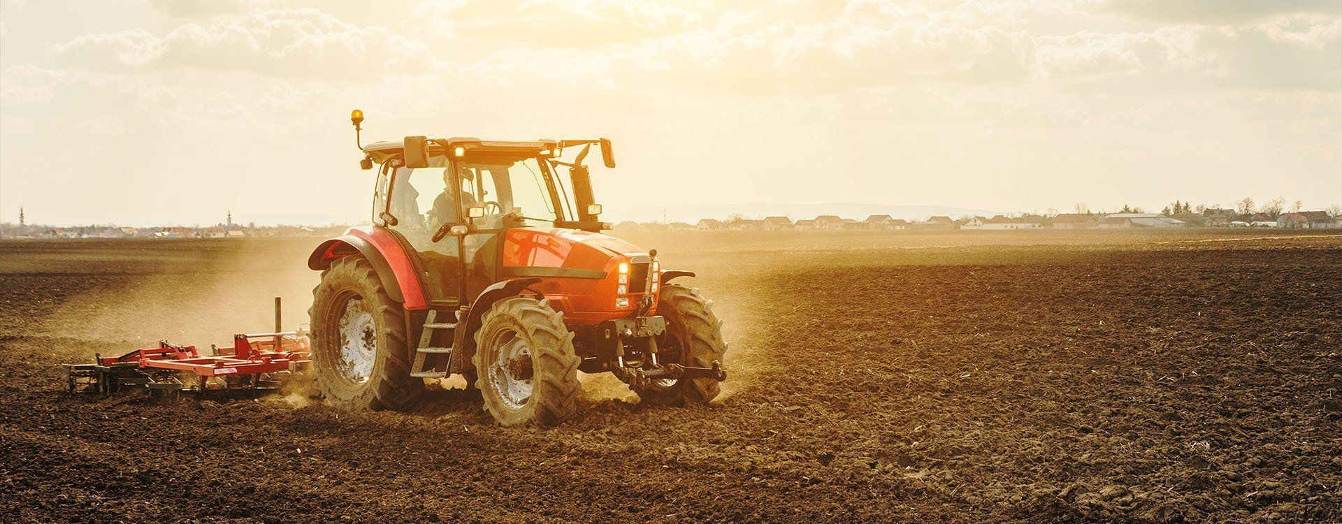 Red Tractor Plowing a Field — Paul’s Tyres & Farm Maintenance in Parkes, NSW