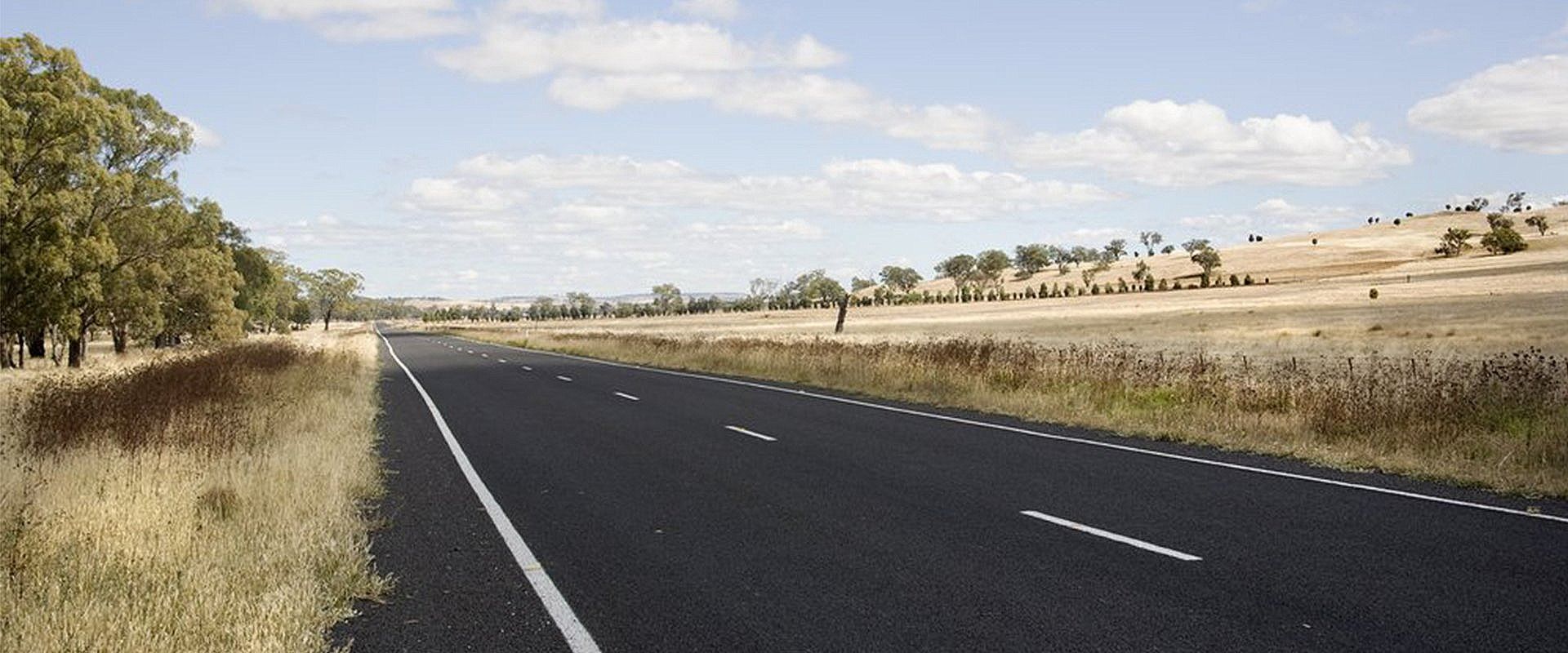 An Asphalt Road Stretches Through a Dry, Grassy Landscape — Paul’s Tyres & Farm Maintenance in Wellington, NSW