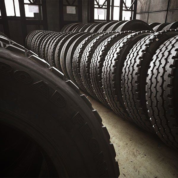Rows of Black Tires Stacked Inside a Dimly Lit Industrial Building — Paul’s Tyres & Farm Maintenance in Parkes, NSW