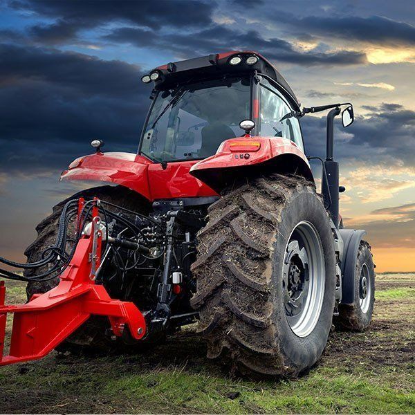 Red Tractor in a Field With Dark Sky — Paul’s Tyres & Farm Maintenance in Apsley, NSW