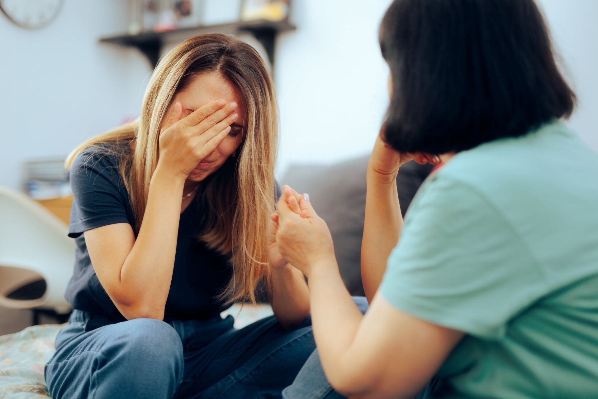 Woman crying, covering her face. Another woman comforts her with a hand on her hand. Inside.