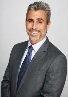A man in a white coat and tie is smiling for the camera.