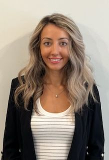 A woman wearing a striped shirt and a black jacket is smiling for the camera.