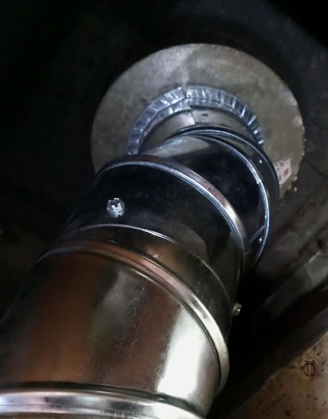 Metal ductwork elbow installed near a ceiling. The elbow is connected to a circular flange, suggesting a ventilation system component.