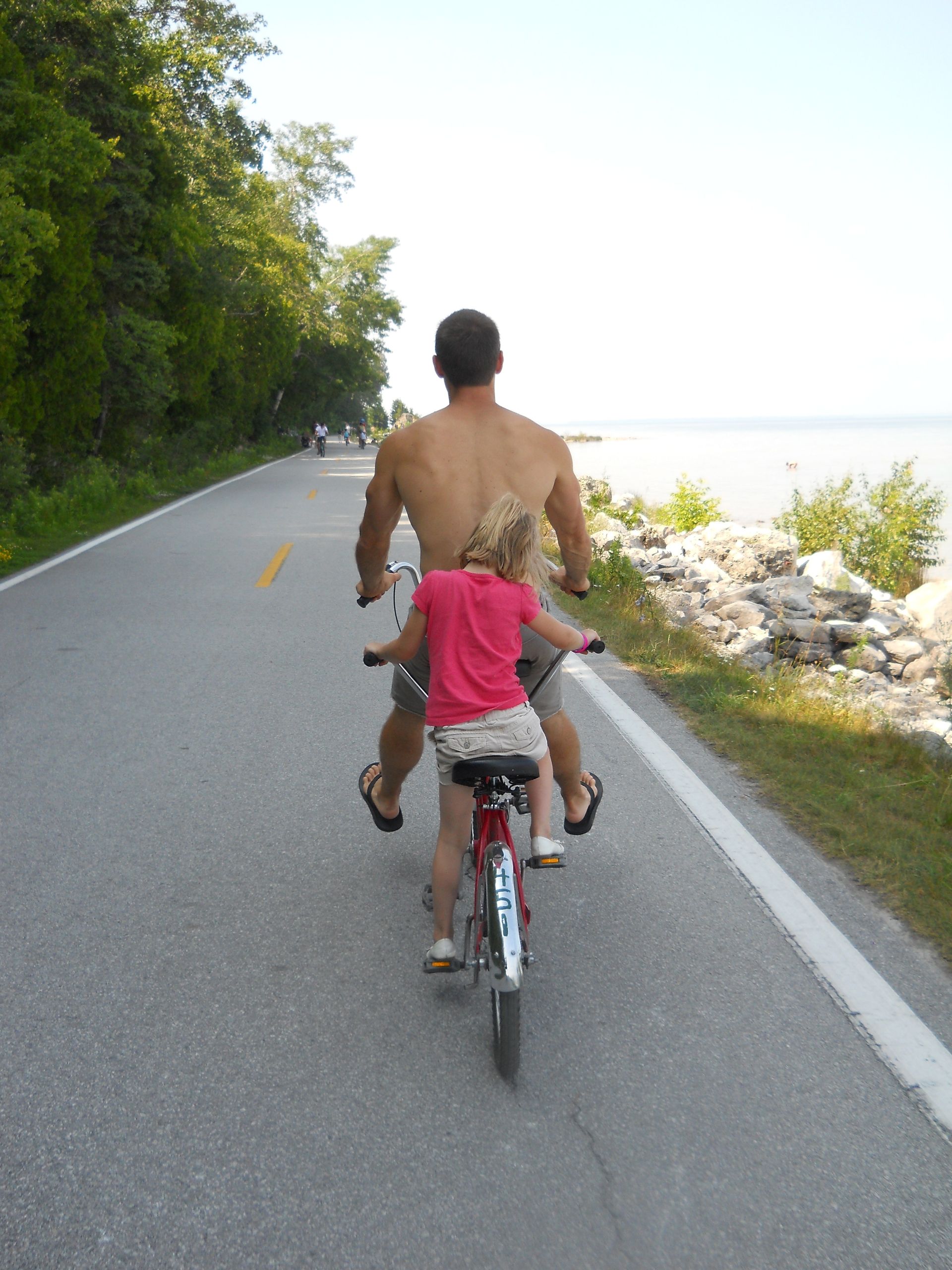 Father and daughter riding a bike together along a path near the water.
