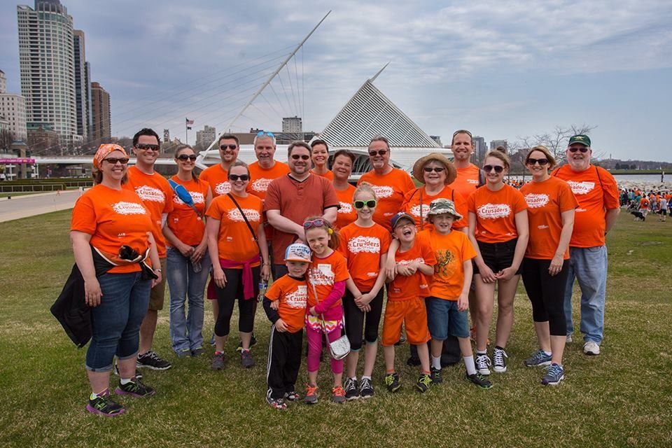 Group of people in orange shirts, walking outdoors near a modern building, likely for a cause.