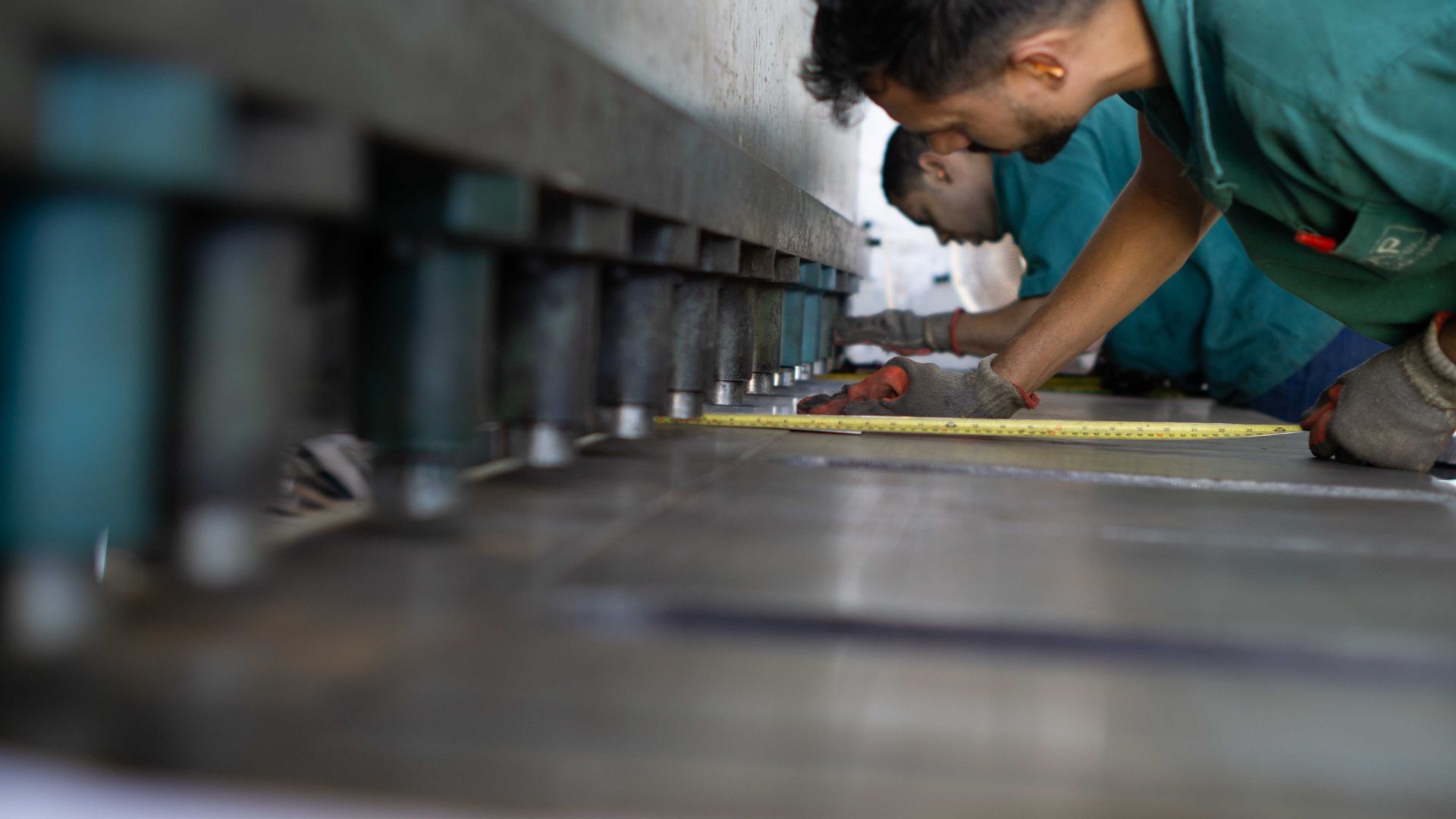 Two men are measuring a piece of metal with a tape measure.