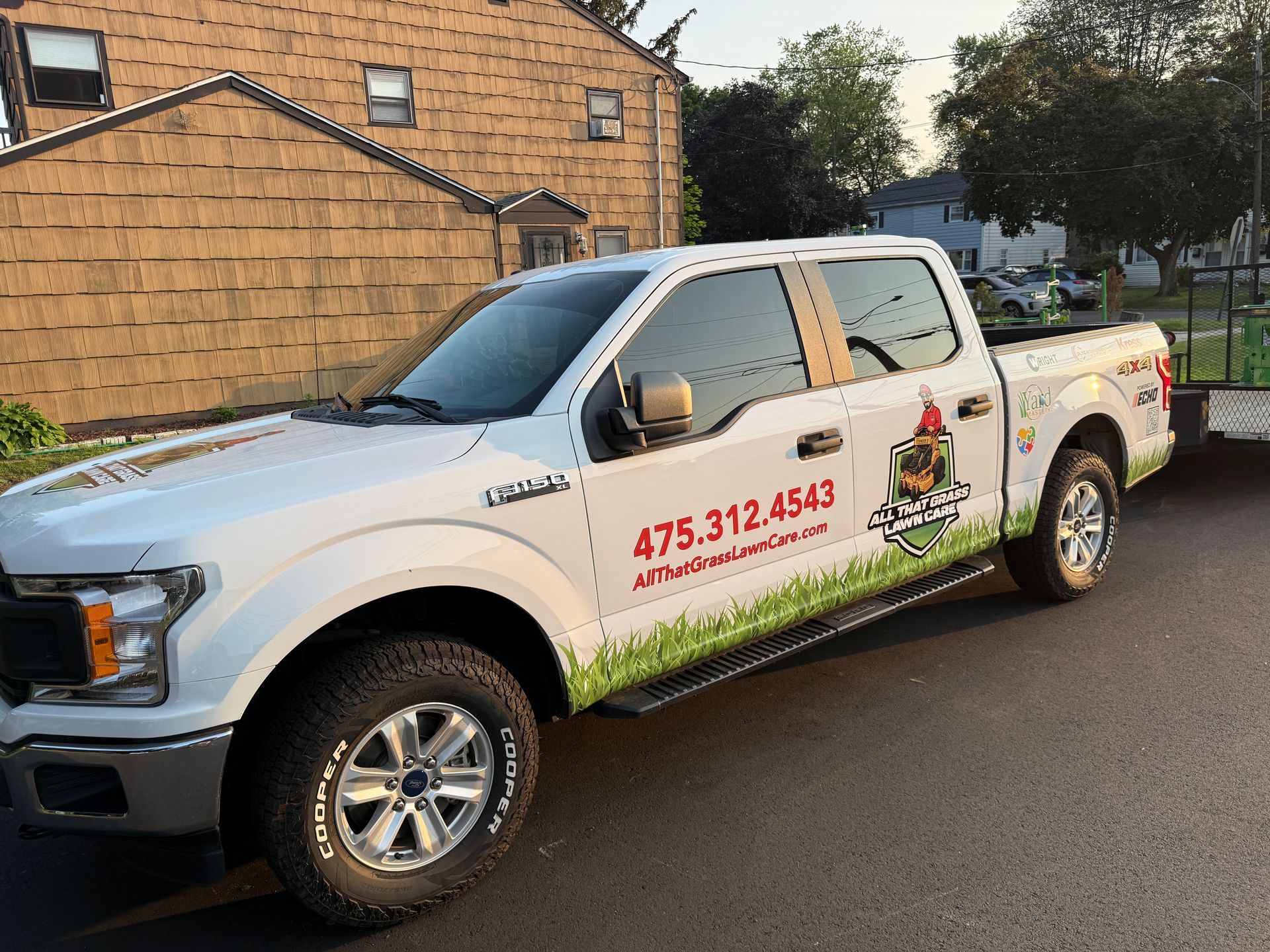 A white truck with a trailer attached to it is parked in front of a house.