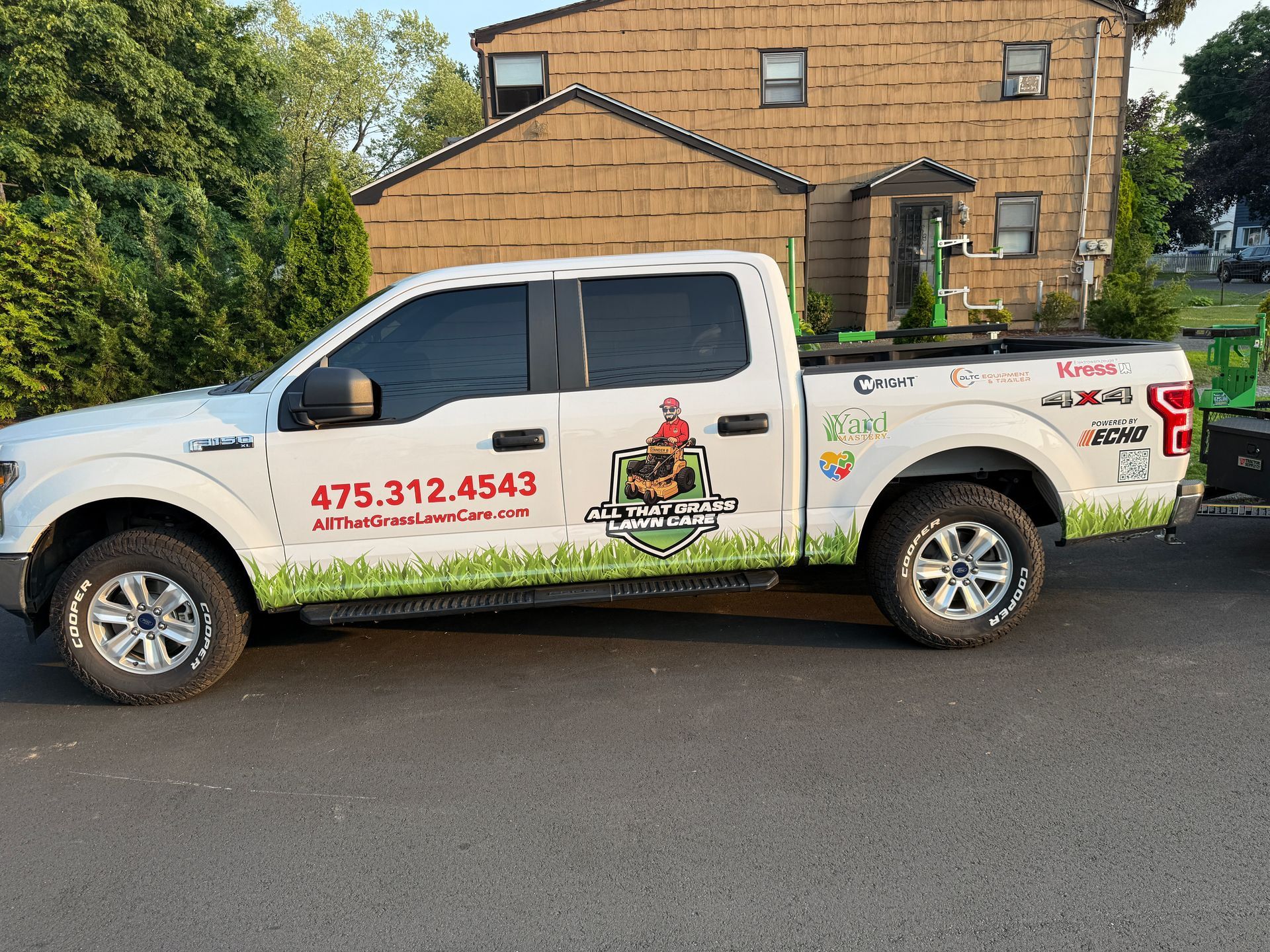 A white truck with a lawn mower on the back is parked in front of a house.