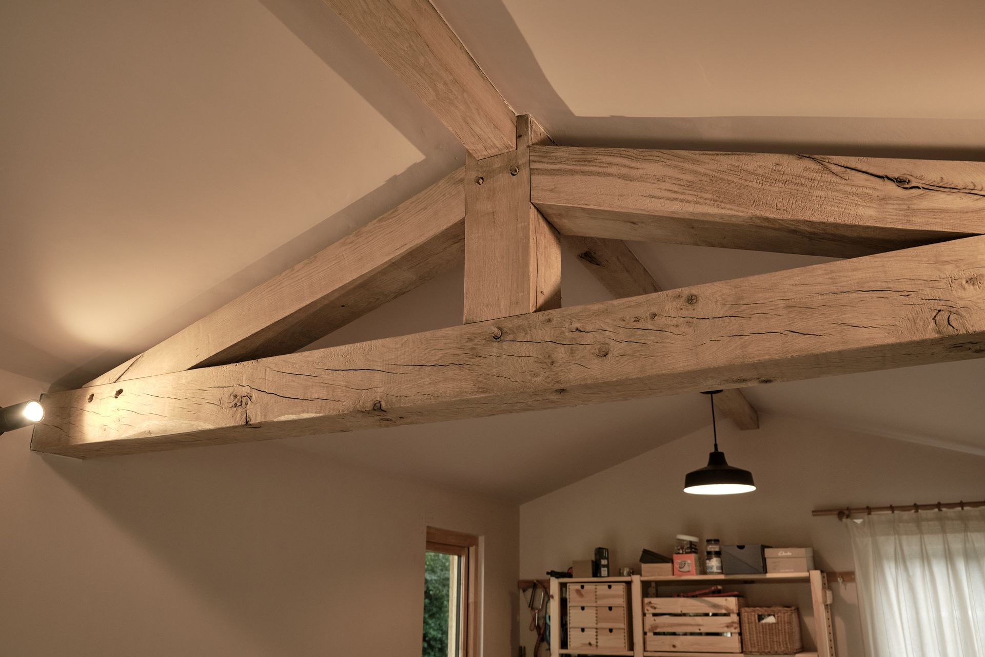 garden room interior with traditional oak framed kingpost truss and exposed ridges, with industrial lighting and storage furniture in the background