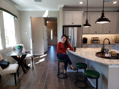 A kitchen with white cabinets , wooden floors , stainless steel appliances and a large island with chairs.