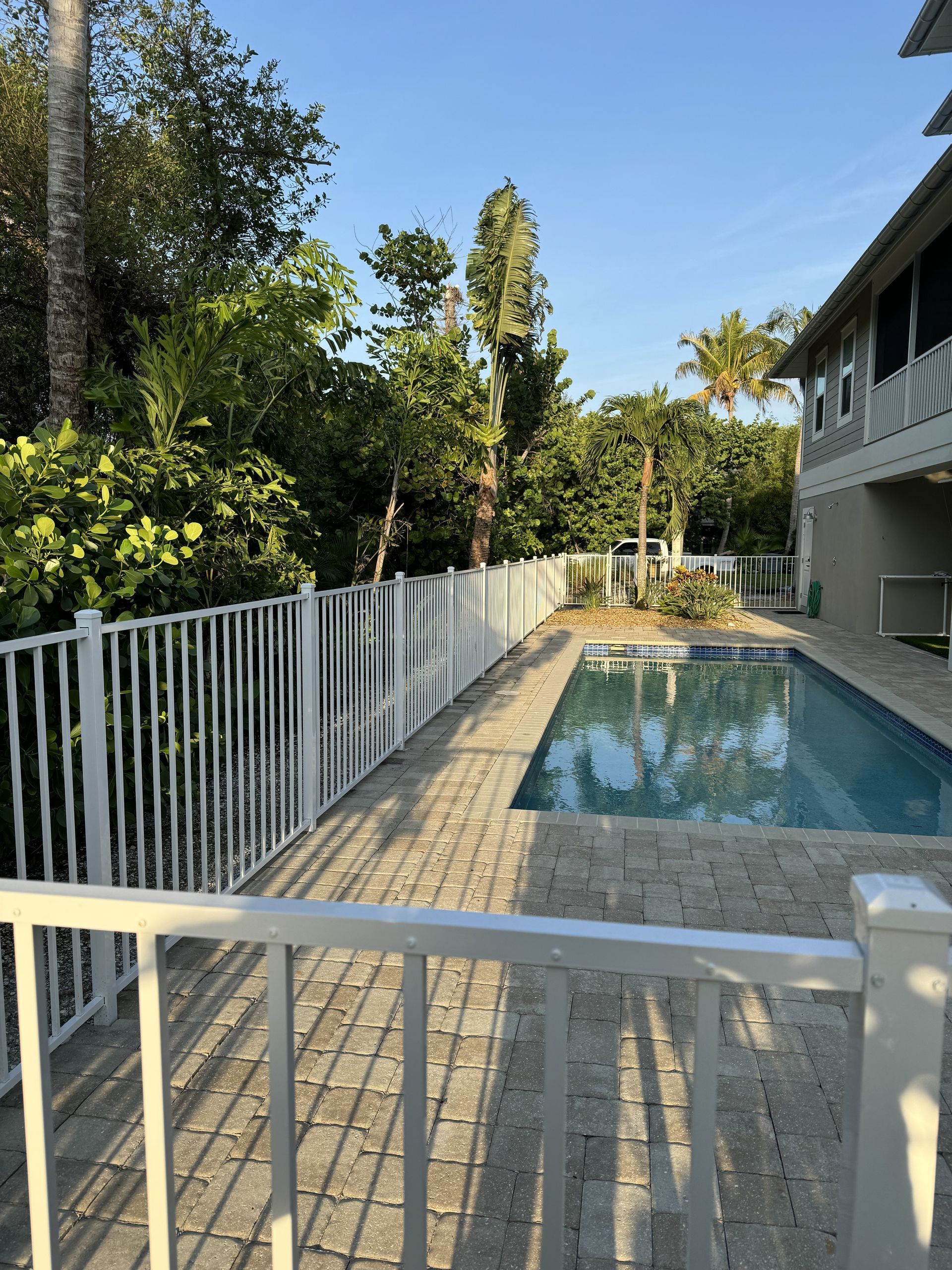 A large swimming pool is surrounded by a white fence.