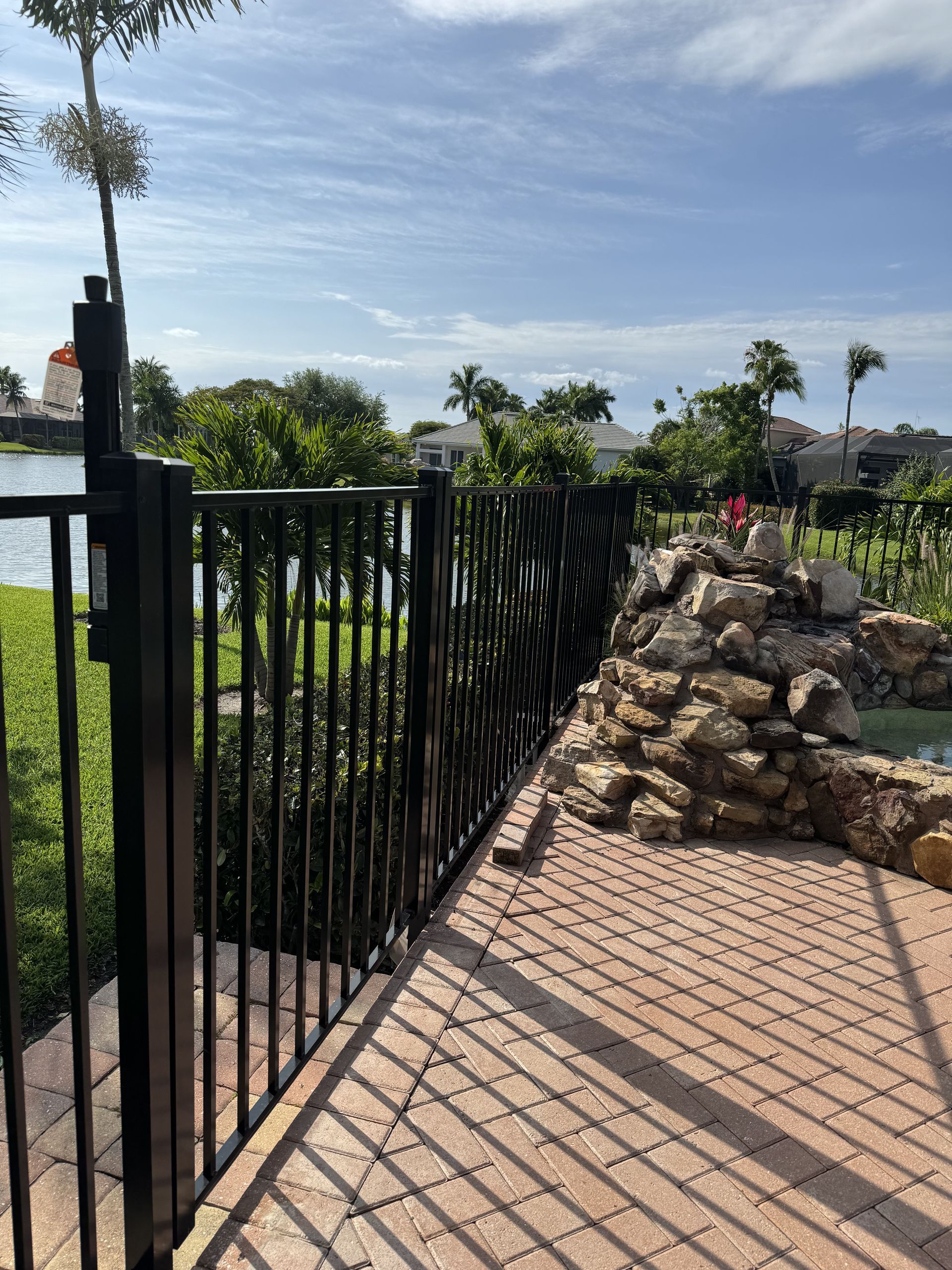 A metal fence surrounds a brick walkway with a waterfall in the background.