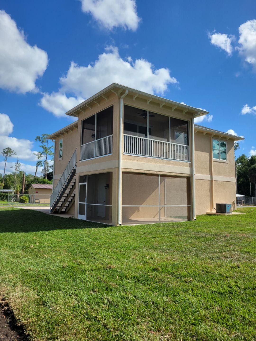 A house with a screened in porch and stairs is sitting on top of a lush green lawn.