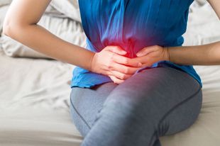 Woman In A Blue Shirt Is Holding Her Stomach In Pain — Naturopath Australia In Mermaid Beach, QLD