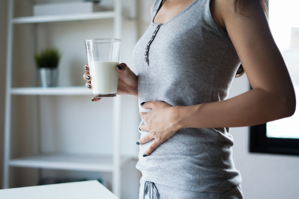 A Woman Is Holding A Glass Of Milk And Holding Her Stomach — Naturopath Australia In Mermaid Beach, QLD