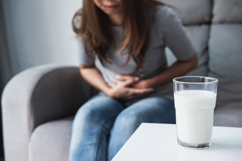 a woman is sitting on a couch with a glass of milk on a table — Herbalism & Naturopathy on Tweed Heads NSW