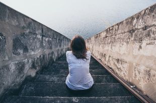 A Depressed Woman Sits On A Set Of Stairs Looking At The Water — Naturopath Australia In Mermaid Beach, QLD