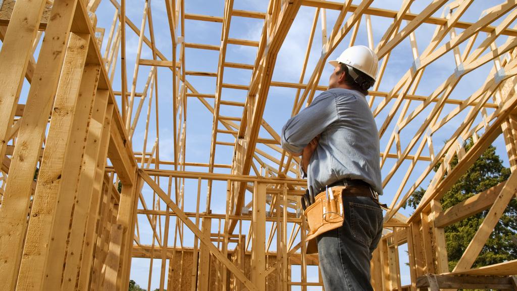 A man wearing a hard hat is standing in front of a wooden structure under construction.