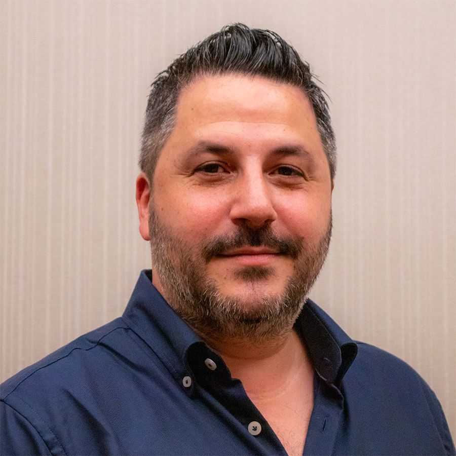 A man with a beard is wearing a blue shirt and smiling for the camera.