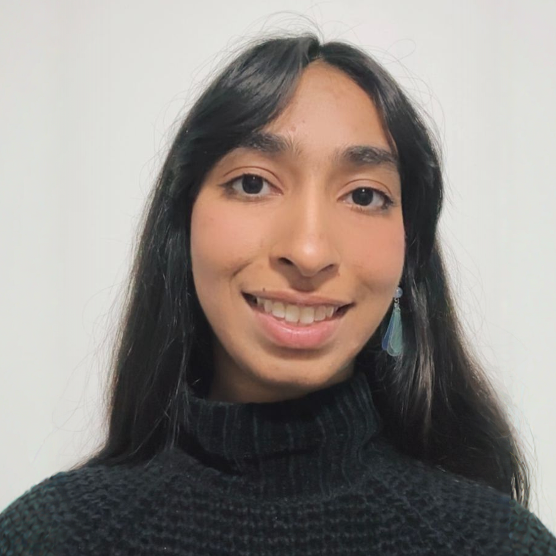 A woman with long dark hair is smiling for the camera while wearing a black sweater.