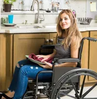 A woman is sitting in a wheelchair in a kitchen.