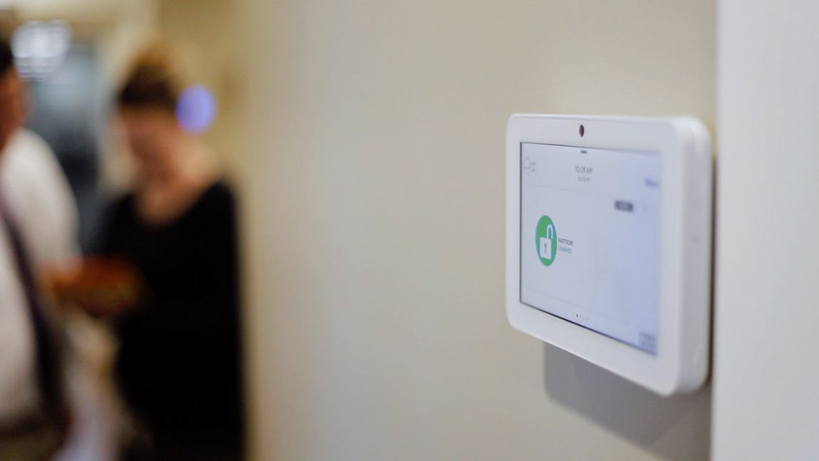 Wall-mounted touchscreen thermostat on a beige wall with a blurred person in the background