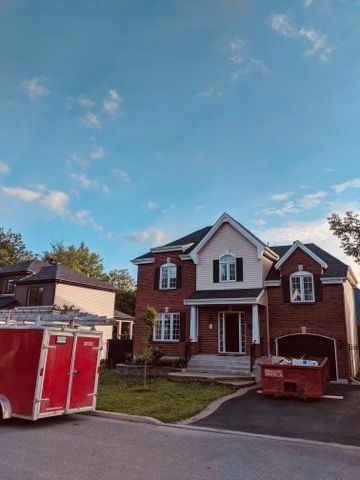 Une remorque rouge est garée devant une grande maison en briques.