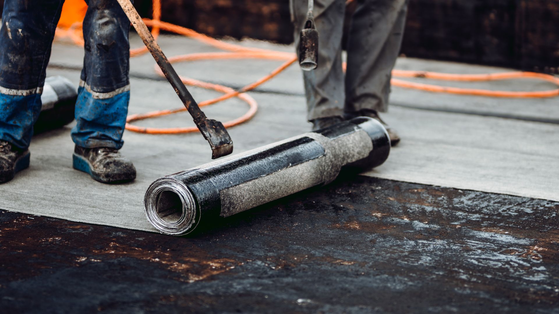 A man is rolling a roll of asphalt on a roof.