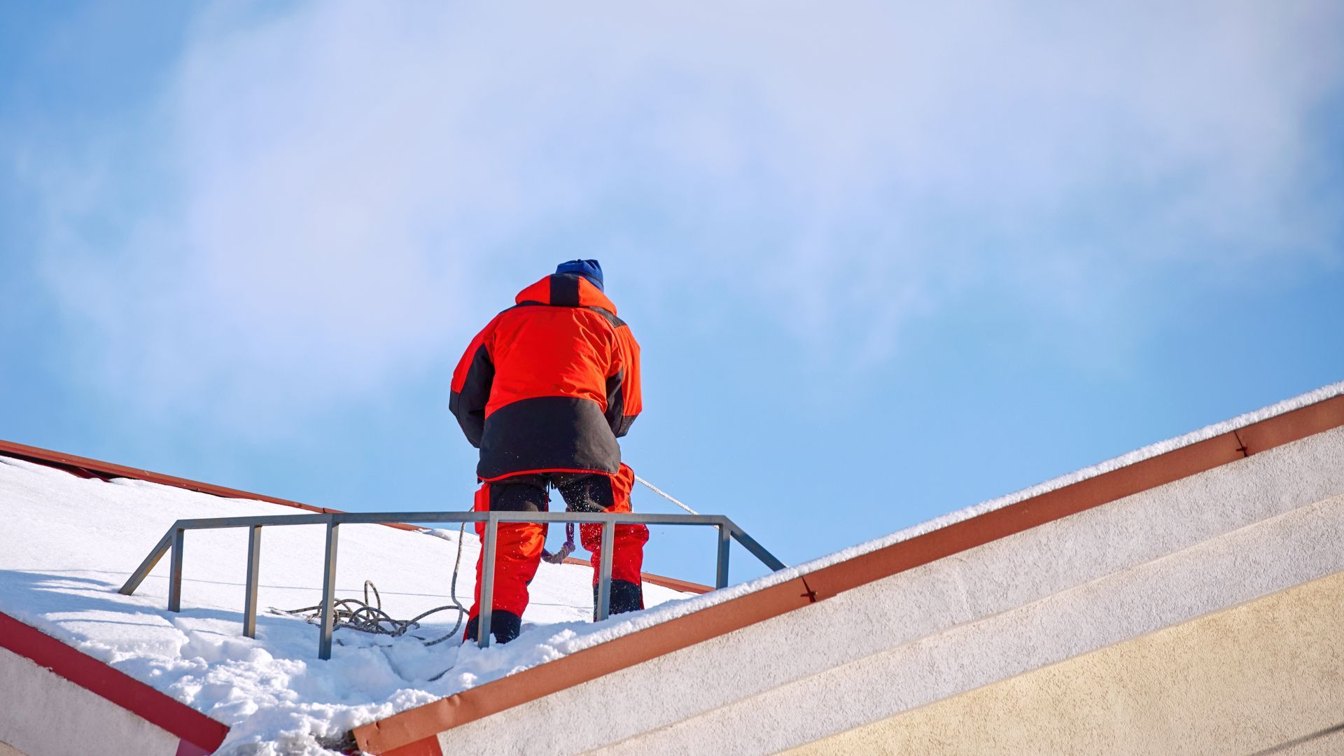 A man is standing on top of a snow covered roof.