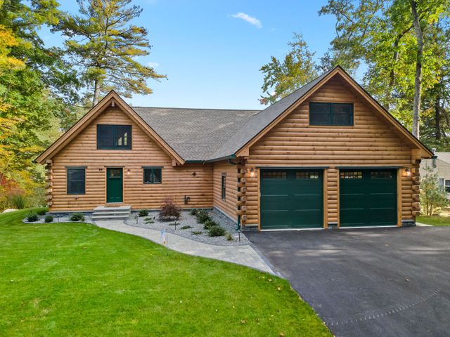 A log cabin with two green garage doors and a driveway