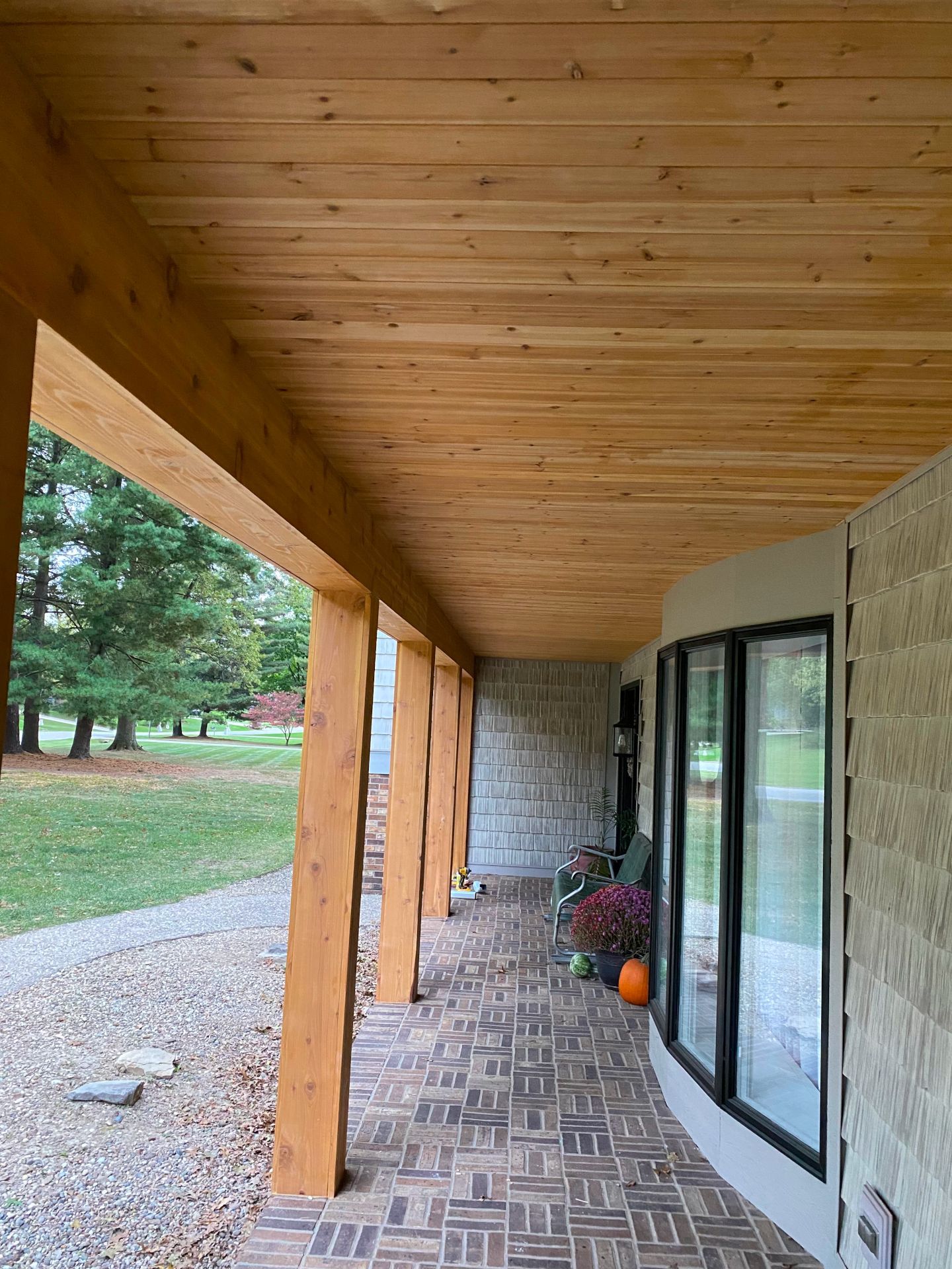 A wooden porch with a brick floor and a wooden ceiling.