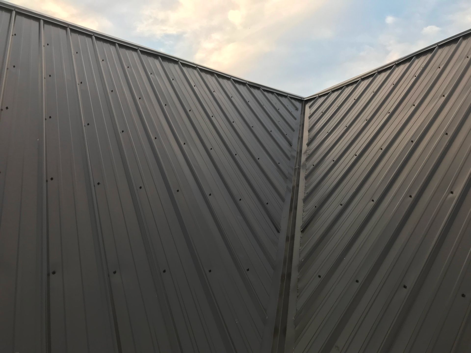 A close up of a metal roof with a cloudy sky in the background.