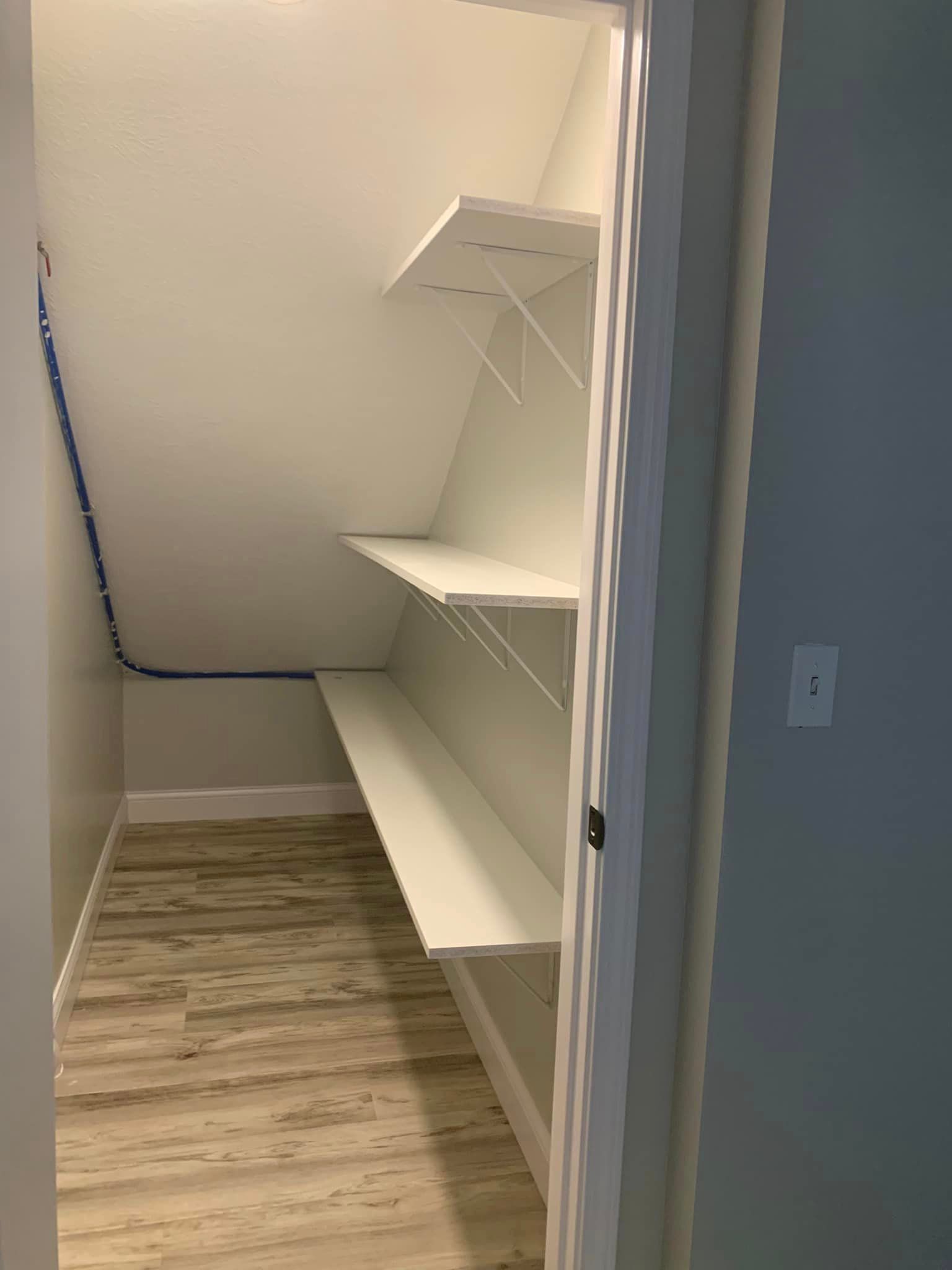 A walk in closet with a slanted ceiling and shelves.