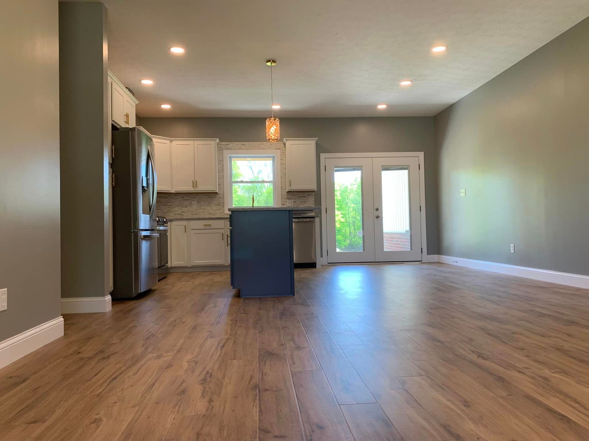 An empty living room with hardwood floors and a kitchen in the background.
