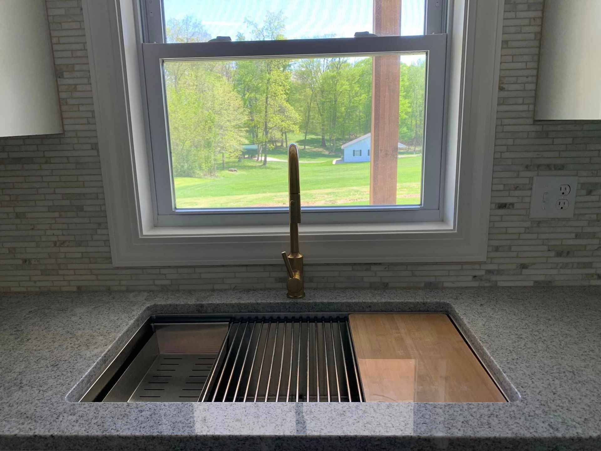 A kitchen sink with a wooden cutting board underneath it and a window.