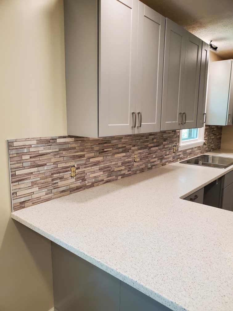 A kitchen with gray cabinets , white counter tops , a sink and a window.